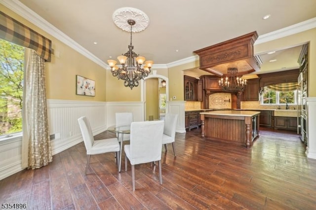 dining space with arched walkways, wainscoting, an inviting chandelier, ornamental molding, and dark wood-type flooring