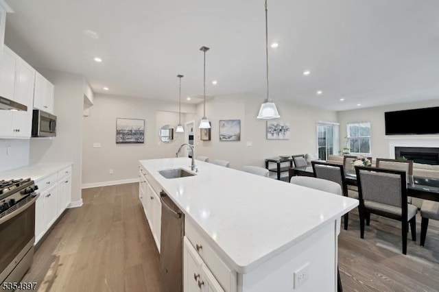 kitchen with appliances with stainless steel finishes, a center island with sink, wood finished floors, a sink, and white cabinetry