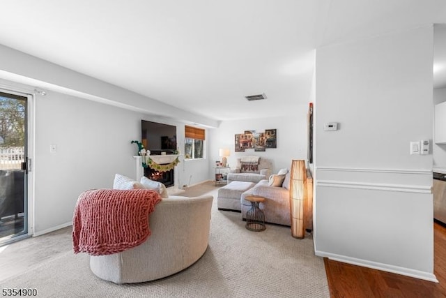 living area featuring visible vents, a warm lit fireplace, baseboards, and a wealth of natural light