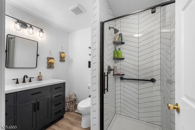 bathroom featuring vanity, toilet, wood finished floors, visible vents, and a stall shower