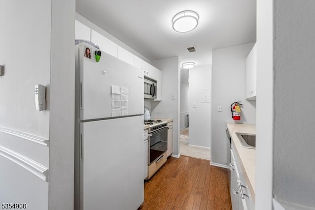 kitchen featuring white cabinets, dark wood finished floors, freestanding refrigerator, stainless steel microwave, and range with gas cooktop