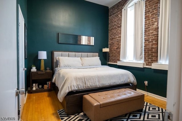 bedroom with brick wall, baseboards, and wood finished floors