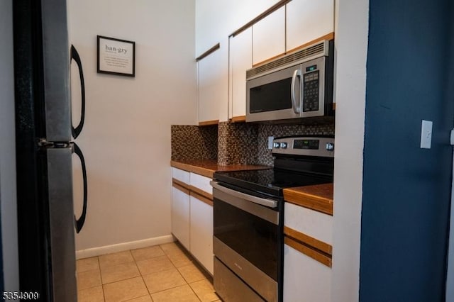 kitchen featuring dark countertops, baseboards, white cabinets, tasteful backsplash, and appliances with stainless steel finishes