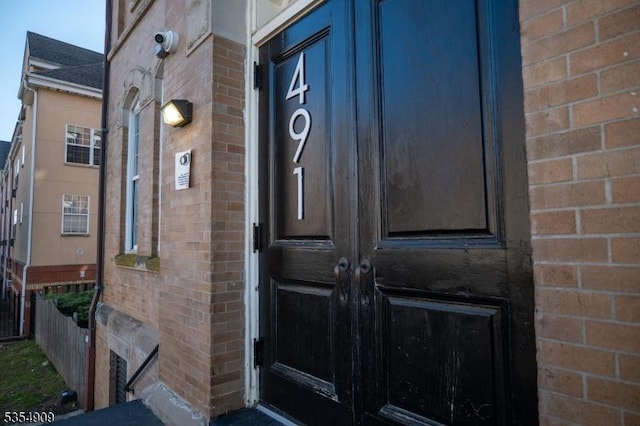 property entrance with roof with shingles, fence, and brick siding