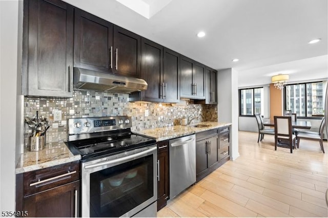 kitchen featuring decorative backsplash, light wood-style floors, under cabinet range hood, light stone counters, and stainless steel appliances