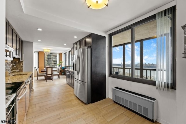 kitchen with light wood-style flooring, appliances with stainless steel finishes, radiator heating unit, and a healthy amount of sunlight