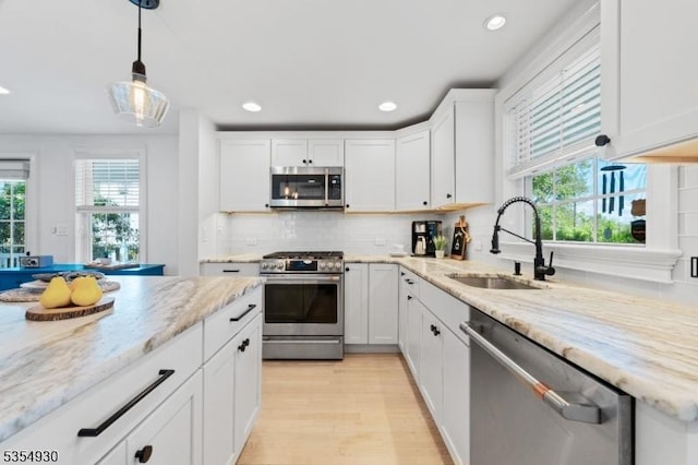kitchen featuring stainless steel appliances, a sink, white cabinets, tasteful backsplash, and hanging light fixtures