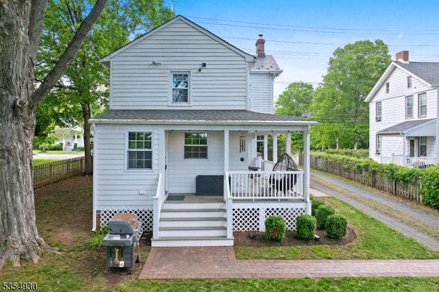 view of front of home with covered porch, fence, a chimney, and a shingled roof