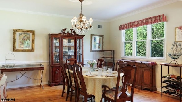 dining space with visible vents, an inviting chandelier, ornamental molding, and light wood finished floors