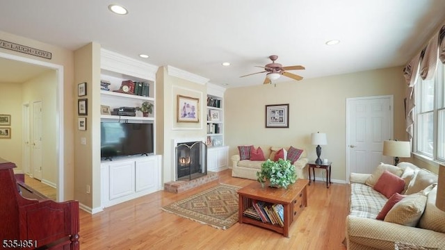 living area with recessed lighting, a ceiling fan, light wood-style flooring, and a lit fireplace