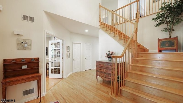 stairs featuring a towering ceiling, recessed lighting, wood finished floors, and visible vents