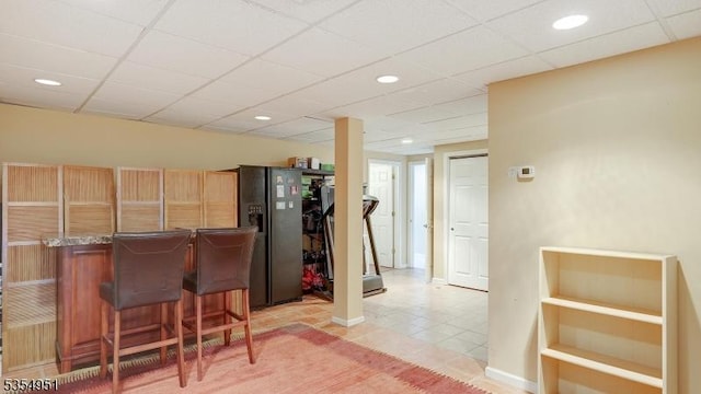 bar with black fridge with ice dispenser, a bar, a drop ceiling, recessed lighting, and light tile patterned flooring