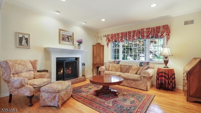 living room with visible vents, wood finished floors, a warm lit fireplace, ornamental molding, and recessed lighting