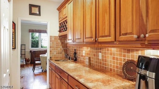 kitchen featuring light stone counters, a sink, brown cabinetry, wood finished floors, and tasteful backsplash