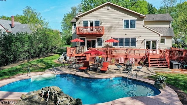 back of property with a wooden deck, an outdoor pool, and a balcony