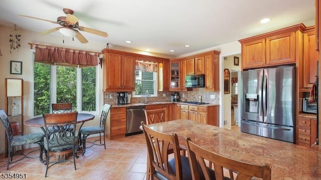 kitchen with appliances with stainless steel finishes, a sink, brown cabinetry, a ceiling fan, and tasteful backsplash