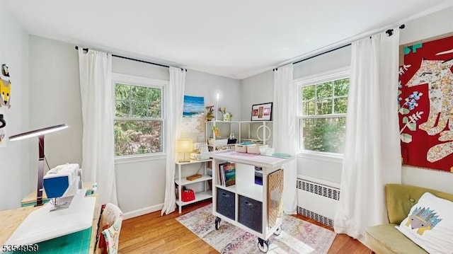 rec room with radiator, plenty of natural light, baseboards, and wood finished floors