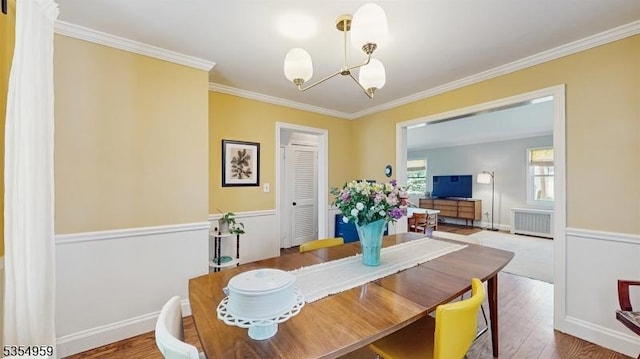dining space with radiator heating unit, an inviting chandelier, wood finished floors, and crown molding
