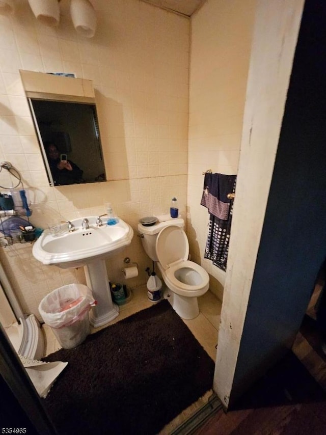 half bath with tile walls, toilet, a sink, and tasteful backsplash
