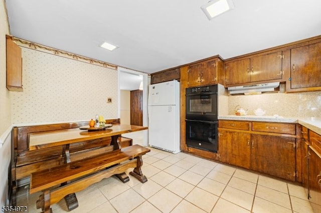 kitchen featuring dobule oven black, freestanding refrigerator, wallpapered walls, light countertops, and under cabinet range hood