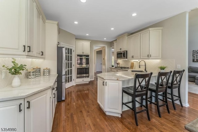 kitchen featuring a peninsula, a sink, stainless steel appliances, dark wood finished floors, and decorative backsplash
