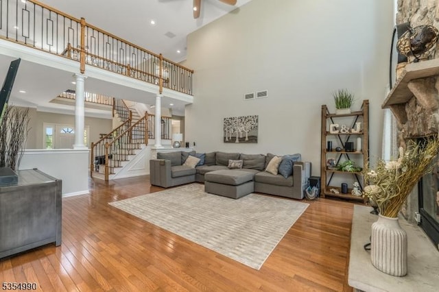 living room featuring a ceiling fan, a high ceiling, decorative columns, visible vents, and hardwood / wood-style flooring