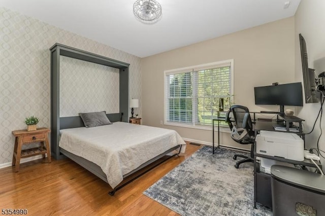bedroom featuring baseboards, wallpapered walls, and light wood-style floors