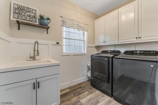 clothes washing area with cabinet space, washer and clothes dryer, light wood finished floors, and a sink