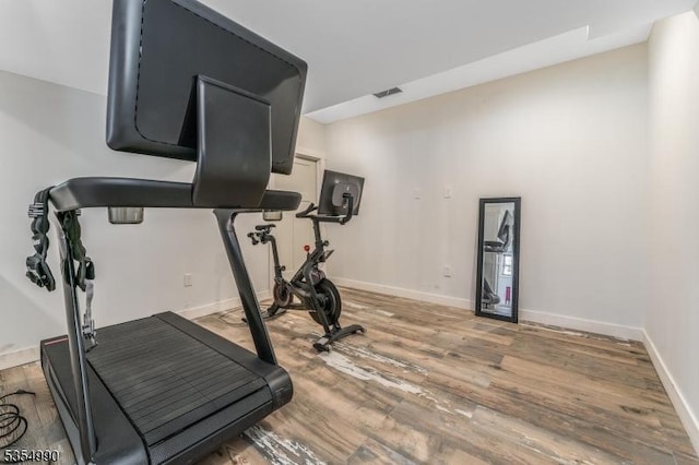 workout area with light wood finished floors, visible vents, and baseboards