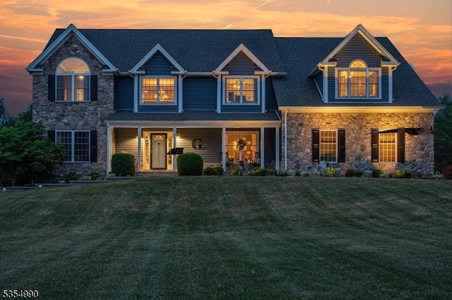 view of front of house featuring covered porch, stone siding, roof with shingles, and a front lawn