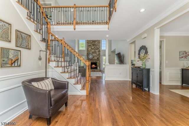 foyer with wood finished floors, a wainscoted wall, a fireplace, ornamental molding, and stairs