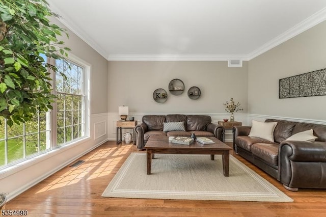 living area featuring wainscoting, ornamental molding, light wood-type flooring, and visible vents