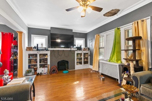 living area featuring a ceiling fan, a fireplace, wood finished floors, radiator, and ornamental molding