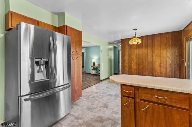 kitchen with stainless steel fridge, light countertops, wooden walls, brown cabinetry, and pendant lighting