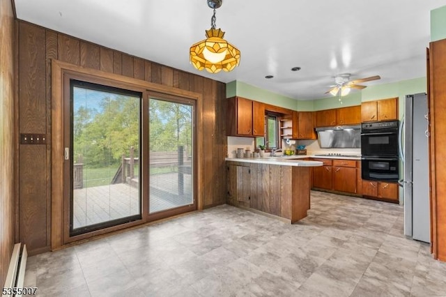 kitchen featuring a peninsula, a baseboard heating unit, freestanding refrigerator, wood walls, and cooktop