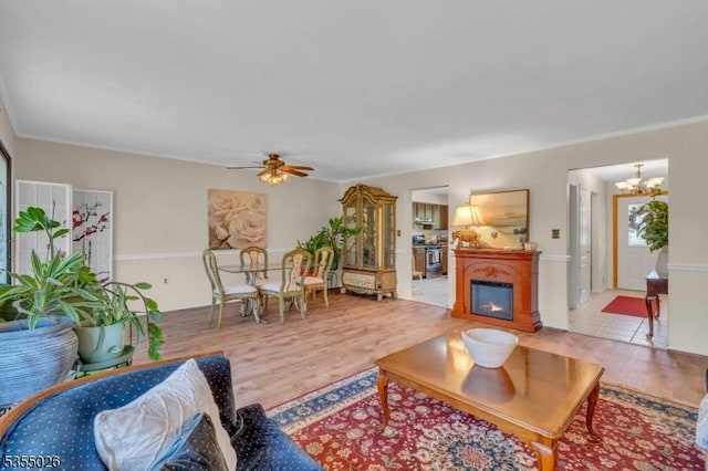 living room with crown molding, wood finished floors, and ceiling fan with notable chandelier