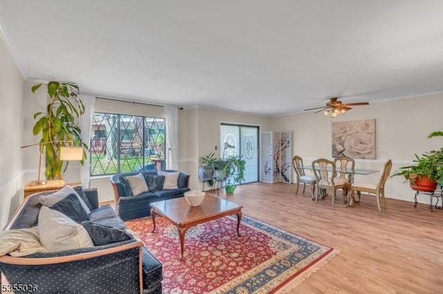 living room with crown molding, a ceiling fan, and light wood-type flooring
