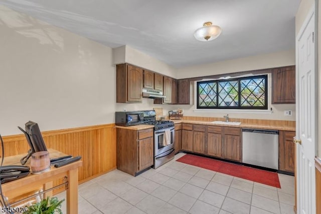 kitchen with a sink, light countertops, stainless steel appliances, and under cabinet range hood
