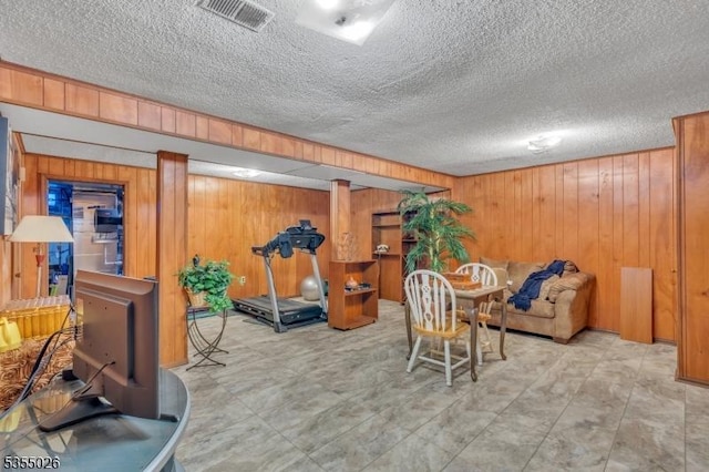 interior space with wooden walls, a textured ceiling, and visible vents