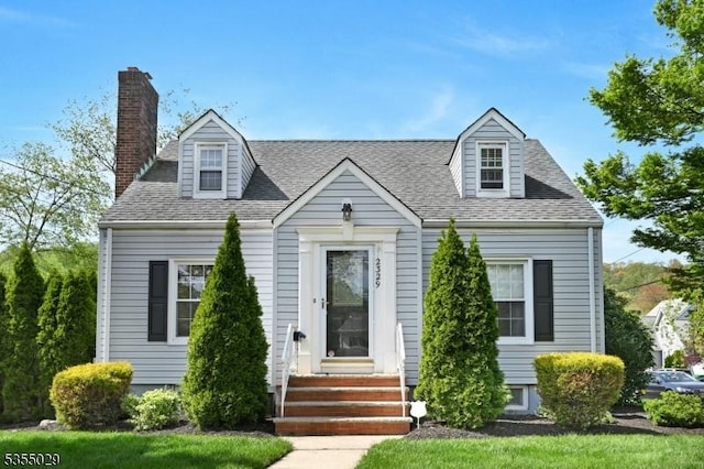 cape cod house featuring roof with shingles, a chimney, and entry steps