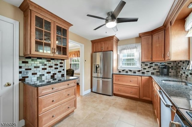 kitchen featuring dark stone counters, appliances with stainless steel finishes, brown cabinetry, and a ceiling fan