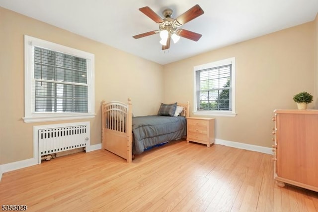 bedroom with baseboards, light wood finished floors, ceiling fan, and radiator heating unit