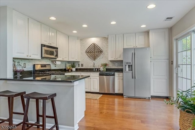 kitchen with light wood finished floors, a peninsula, white cabinetry, and stainless steel appliances