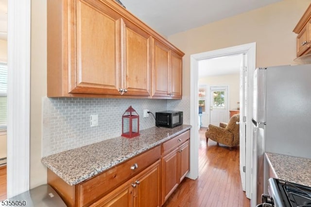 kitchen with freestanding refrigerator, light wood-style flooring, backsplash, and black microwave