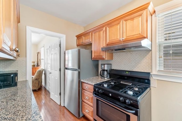 kitchen featuring appliances with stainless steel finishes, under cabinet range hood, tasteful backsplash, and light wood-style flooring