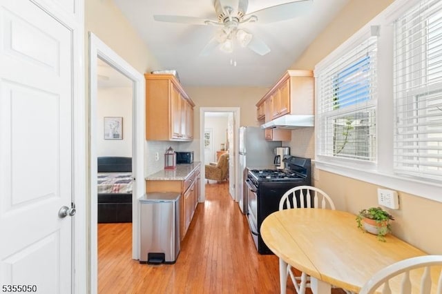 kitchen with stainless steel range with gas cooktop, under cabinet range hood, light wood-style floors, backsplash, and ceiling fan