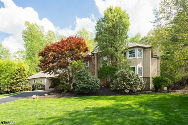 view of front of home with stone siding, driveway, a front lawn, and stucco siding