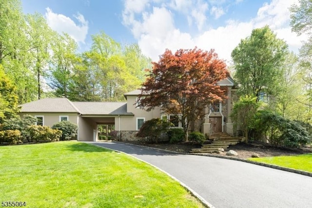 obstructed view of property with a front yard, driveway, stucco siding, an attached carport, and stone siding