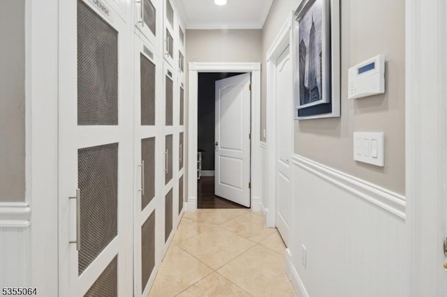 hallway with crown molding, light tile patterned floors, a decorative wall, and wainscoting