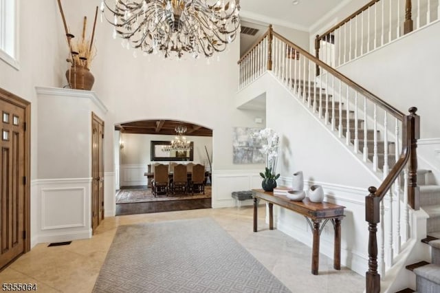 tiled foyer featuring a chandelier, stairway, a decorative wall, a high ceiling, and arched walkways
